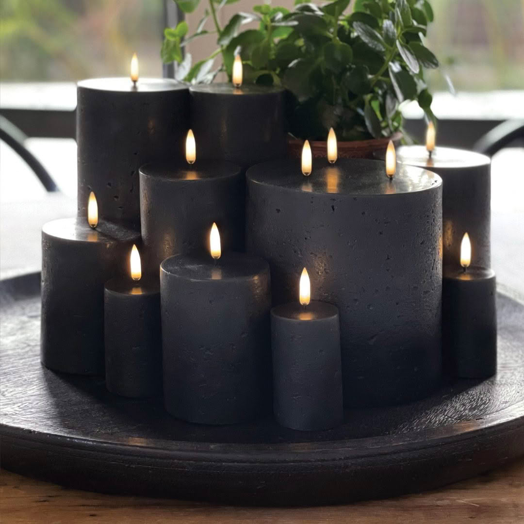 Black candles lit on tray with green plant