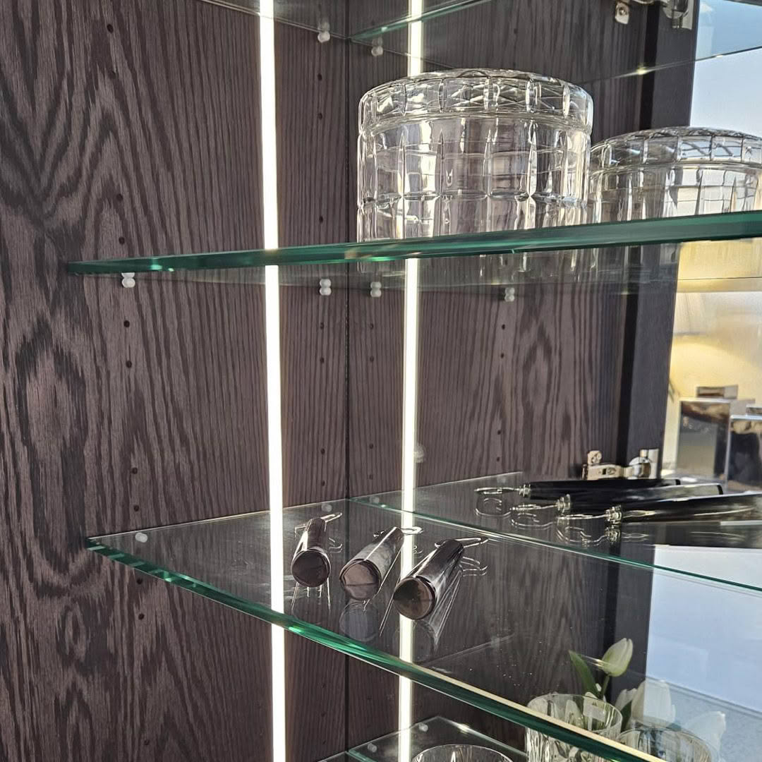 Glass shelves displaying glasses and silverware in cabinet