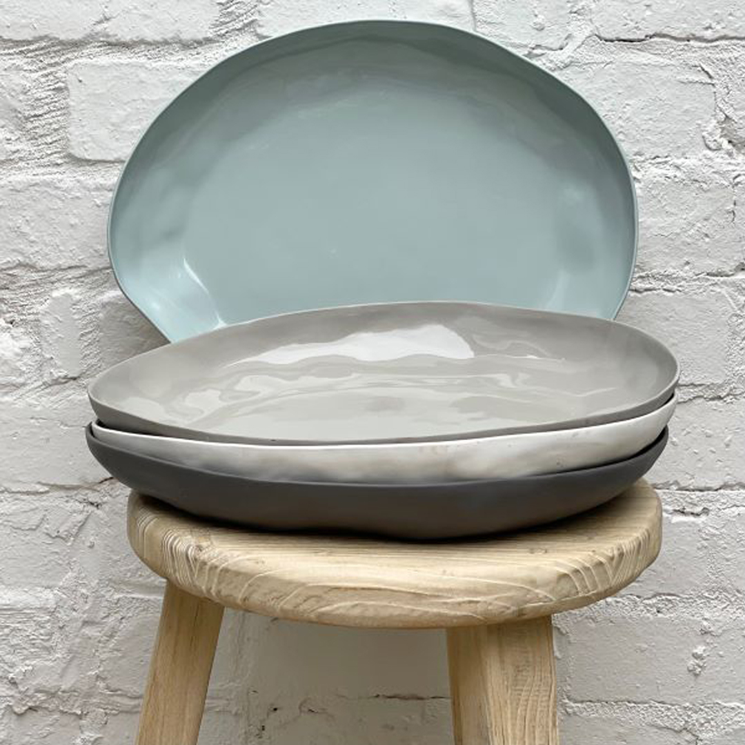 Stacked ceramic plates on wooden stool against brick wall